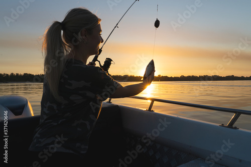 A woman on a fishing trip caught a fish.Fishing on the lake from a boat. Fishing rods in sunlight. Fishing rest concept.