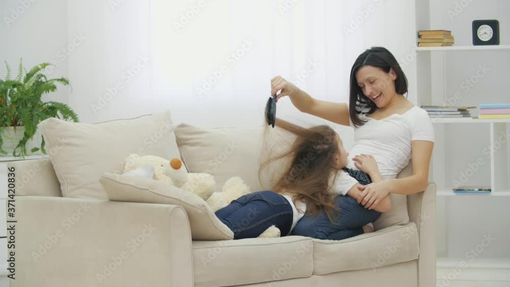 Littlle daughter is lying on mother's legs while mother is combing her hair, smiling, doing crazy hairdo. Littlle daughter is lying on mother's legs while mother is combing her hair, smiling, doing crazy hairdo.