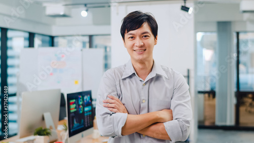 Portrait of successful handsome executive businessman smart casual wear looking at camera and smiling, arms crossed in modern office workplace. Young Asia guy standing in contemporary meeting room.