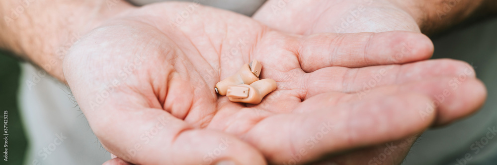 small intra channel hearing aid device in a man's hands. banner small intra channel hearing aid device in a man's hands. banner