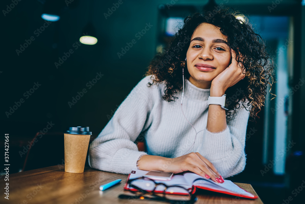 Carefree female meloman looking at camera resting at coffee shop enjoying media playlist with high volume via earphones,portrait of cheerful hipster girl listening positive audio record via headphones Carefree female meloman looking at camera resting at coffee shop enjoying media playlist with high volume via earphones,portrait of cheerful hipster girl listening positive audio record via headphones