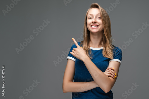 Young woman with blonde straight hair over isolated gray background pointing finger to the side. Presenting your product