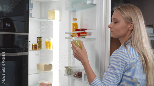 Young blonde woman taking drink from fridge in kitchen at home