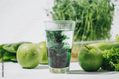 Photos chlorophyll in a glass of water on a white background near are various fresh veg