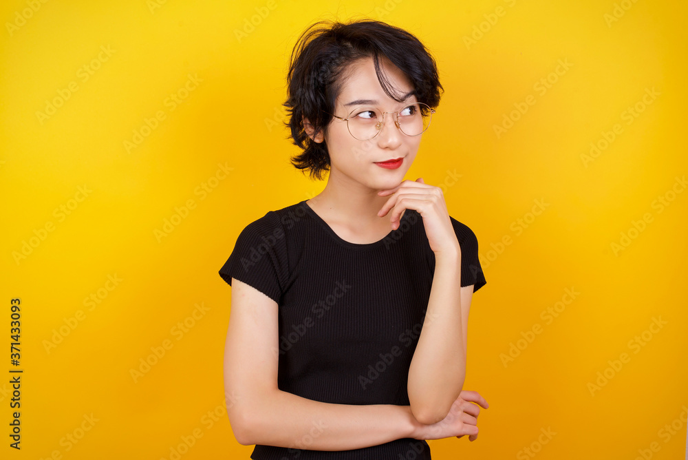 Obraz premium Dreamy female with pleasant expression, wearing casual clothes, looks sideways, keeps hand under chin, thinks about something pleasant, poses against gray background.
