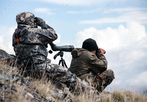 Hunting  in the  mountains determine trophy quality animals through binoculars and a telescope.