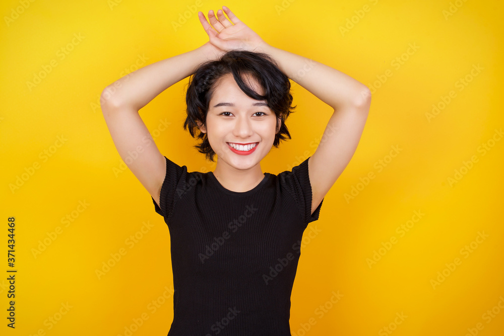 Fototapeta premium Portrait of beautiful brunette female looks with excitement at camera, keeps hands raised over head notices something unexpected, isolated over gray wall. Lovely woman reacts on sudden news.