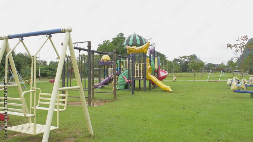 Colorful children's playground on yard in the public park. Swing moves without people. Children stayed home during the Covid 19 pandemic. Slide shot. Colorful children's playground on yard in the public park. Swing moves without people. Children stayed home during the Covid 19 pandemic. Slide shot.