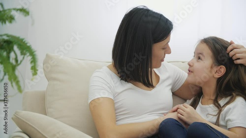 4k video of mother and her daughter talking and sharing secrets sitting on sofa at home.