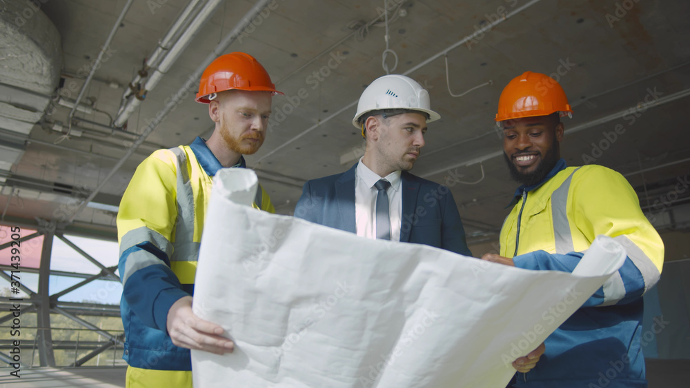 Young engineer discussing blueprint with building workers on construction site Young engineer discussing blueprint with building workers on construction site