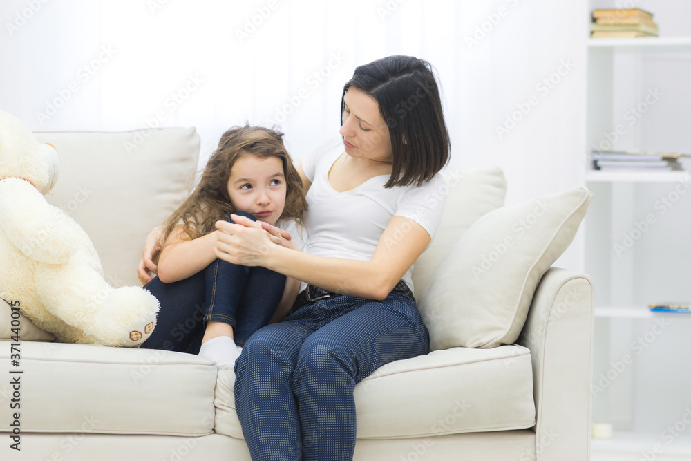 Photo of sad little girl sitting on the sofa and her mom hugging her. Photo of sad little girl sitting on the sofa and her mom hugging her.