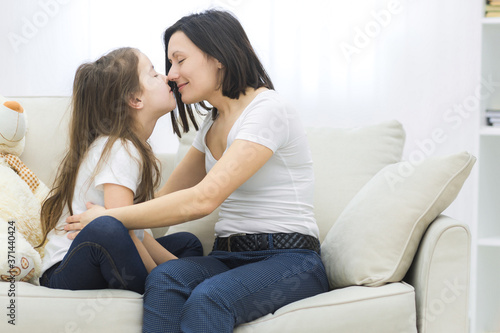 Young woman kissing little girl while sitting in bedroom.