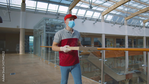 Deliveryman in face protective mask and gloves with pizza box in office building