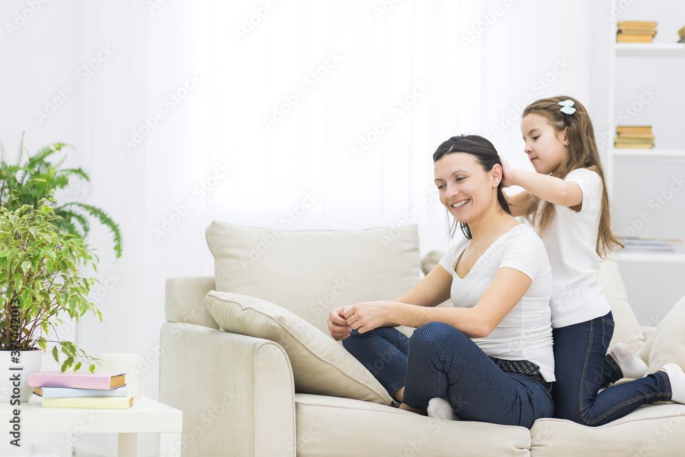 Photo of smiling mom with short dark hair and her beautiful little daughter who is brushing her hair.