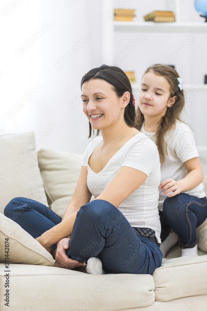 Happy smiling mother and daughter sitting on sofa.