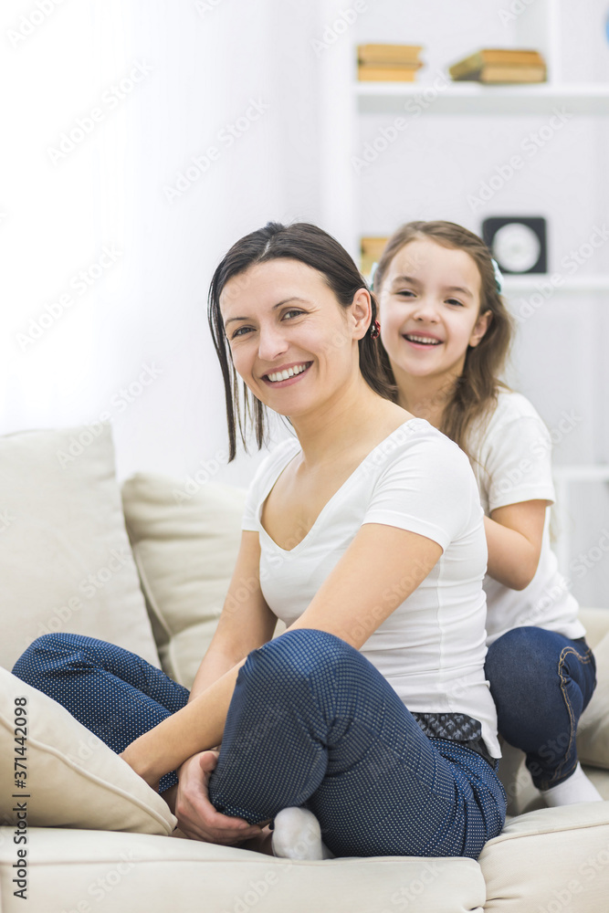 Happy smiling mother and daughter sitting on sofa.