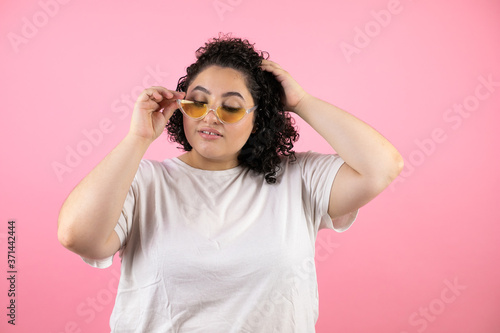 Young beautiful woman wearing sunglasses over isolated pink background smiling and taking and lowering her sunglasses