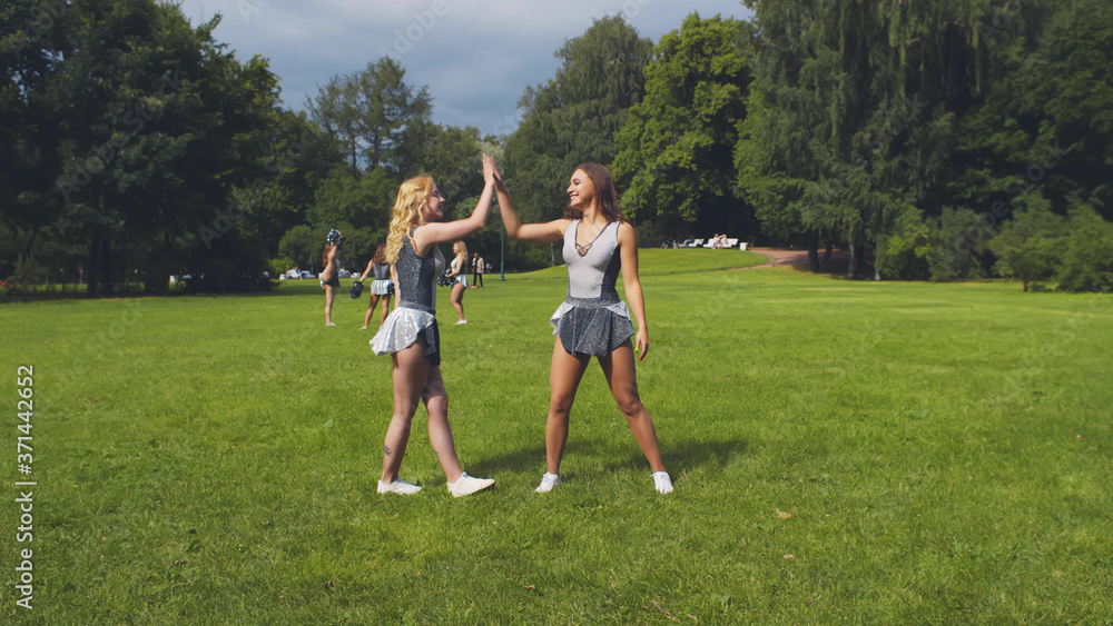 Cheerleader girlfriends giving each other high-five training outdoors