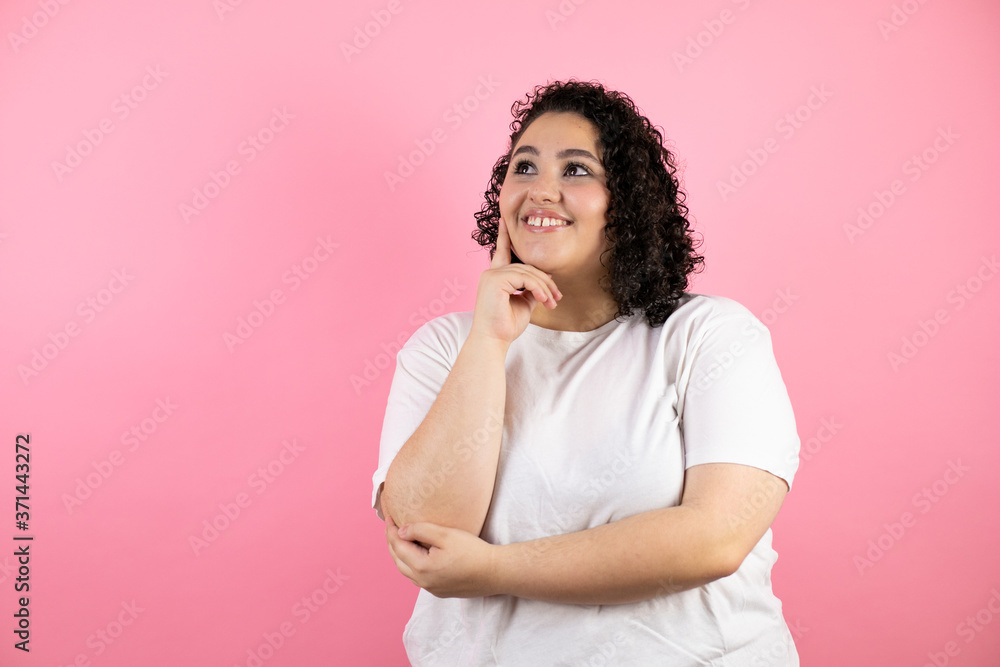 Young beautiful woman standing over isolated pink background looking side confident, smiling with crossed arms and hand raised on chin Young beautiful woman standing over isolated pink background looking side confident, smiling with crossed arms and hand raised on chin