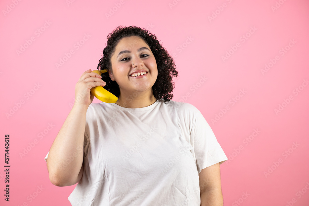 Young beautiful woman over isolated pink background smiling and using a banana as a phone Young beautiful woman over isolated pink background smiling and using a banana as a phone