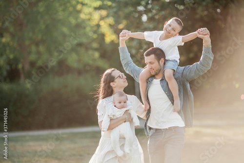 Young beautiful family walks in the park. Family portrait in the sunset light. Summer picnic.