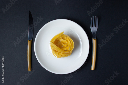 nests of pasta on a black background. Italian pasta. The pasta nest lies on a white plate Nearby cutlery. European cuisine