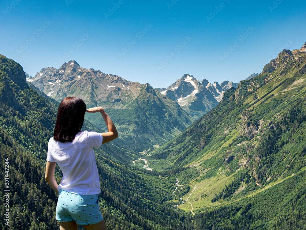 Young girl enjoys a beautiful view of the mountains and blue sky from a height.
