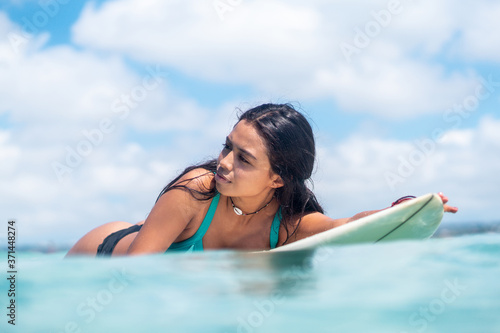 Portrait of surfer girl on white surf board in blue ocean pictured from the water in Bali © Lila Koan