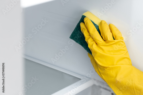 Hand of a woman in yellow glove cleaning the fridge shelf
