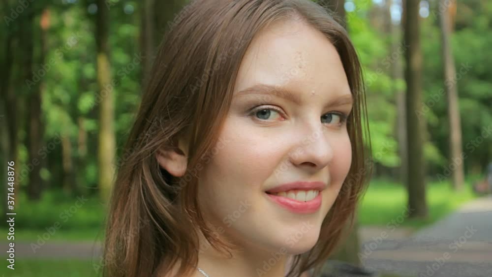 A model poses against a background of trees in sunny weather right in front of the camera. Cute smiles in the park. A model poses against a background of trees in sunny weather right in front of the camera. Cute smiles in the park.