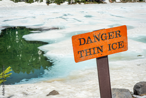 Fényképezés Thin ice warning notice on orange danger signboard by mountain lake
