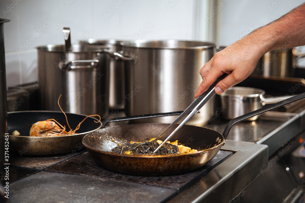 Chef cooking black pasta in a pan with tongs Chef cooking black pasta in a pan with tongs