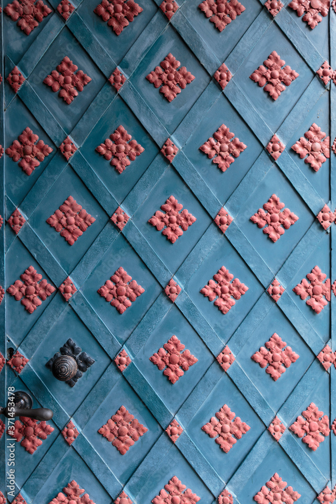 Vertical closeup of a centuries-old, richly ornamented, blue and pink closed front door of an abbey in the German state of Brandenburg