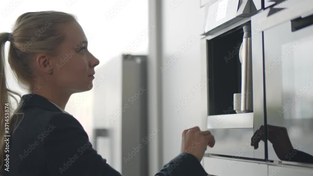 Businesswoman making coffee in coffee machine standing in office kitchen during break Businesswoman making coffee in coffee machine standing in office kitchen during break