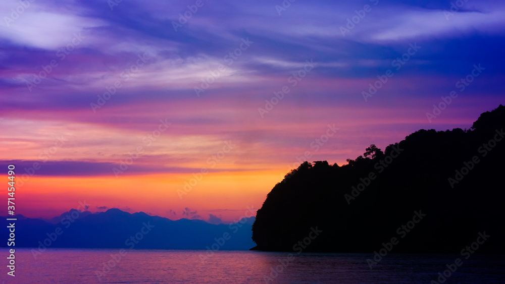 A beautiful setting sun behind the silhouette hills and rocks with its reflection over the sea waves at Tanjung Rhu Beach, Langkawi,