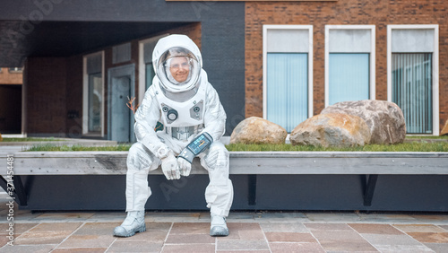 Happy Man in Spacesuit is Sitting on Wooden Bench. Posittive Astronaut Looks in the Distance. Emotionally Joyful Spaceman in White Futuristic Suit with Technological Panel on His Hand. photo