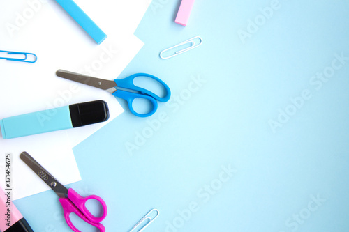 White sheets of paper, colorful markers, erasers, clips and scissors on blue background with space for text. School stationery and supplies. Colorful set of stationery for girls. Back to school