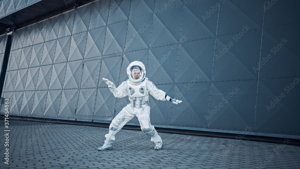 Handsome Man in Spacesuit is Dancing Next to Metal Wall. Astronaut is Happy and Makes Creative Robotic Moves. Successful Spaceman in White Futuristic Suit with Technological Panel on His Hand.