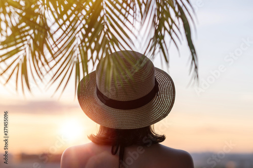 Back view of lonely sad woman in straw hat standing opposite the setting sun over the horizon of the sea. © flowertiare