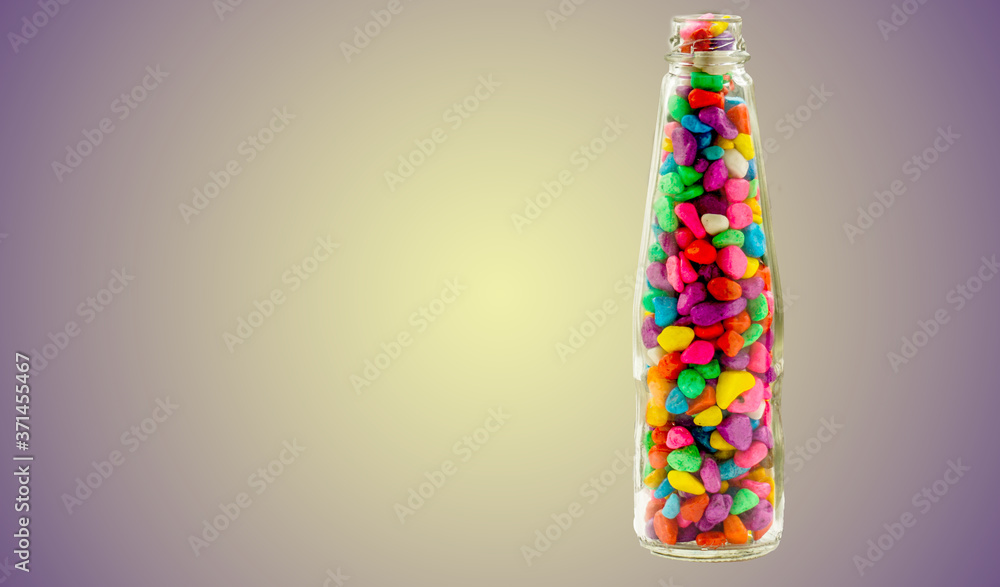 Lovely colorful small pebbles with pink, blue, green, grey and white pebbles in a clear glass bottle with a light violet shaded background.. Lovely colorful small pebbles with pink, blue, green, grey and white pebbles in a clear glass bottle with a light violet shaded background..