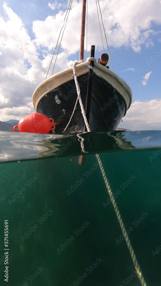 Underwater split photo of traditional classic wooden fishing boat anchored in tropical exotic emerald sea with beautiful sky and clouds