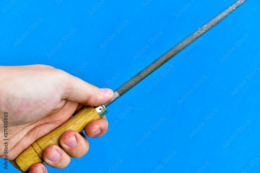 Fototapeta premium Iron round file with wooden handle in hand on blue background