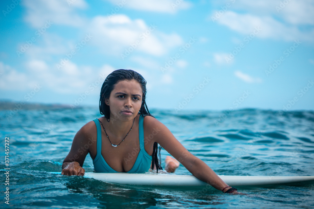 Portrait of surfer girl on white surf board in blue ocean pictured from the water