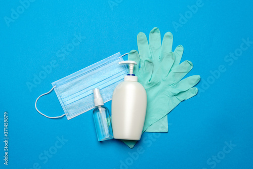 Disposable blue medical face mask, rubber latex gloves and alcohol hand sanitizer antiseptic on blue background
