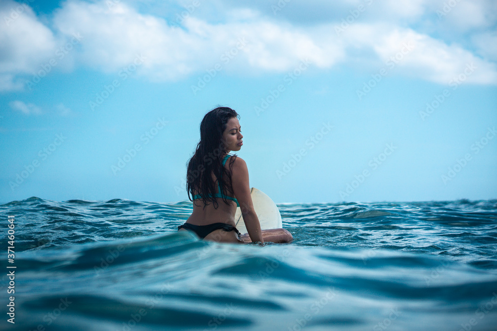 Portrait of surfer girl on white surf board in blue ocean pictured from the water Portrait of surfer girl on white surf board in blue ocean pictured from the water