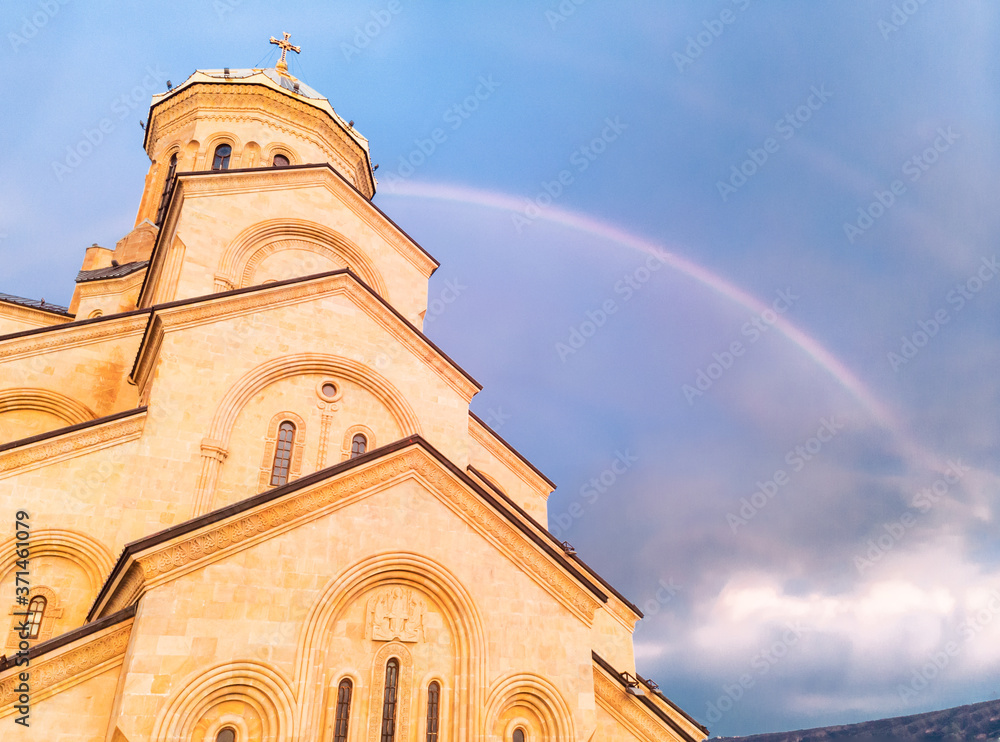 Naklejka premium Close up view of the Sameba holy trinity cathedral with dark blue sky and rainbow in the background. Religion and historical sites in Georgia.