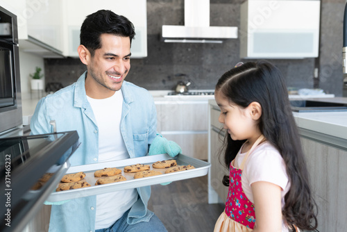 Girl Looking At Father Taking Cookies Out Of Oven