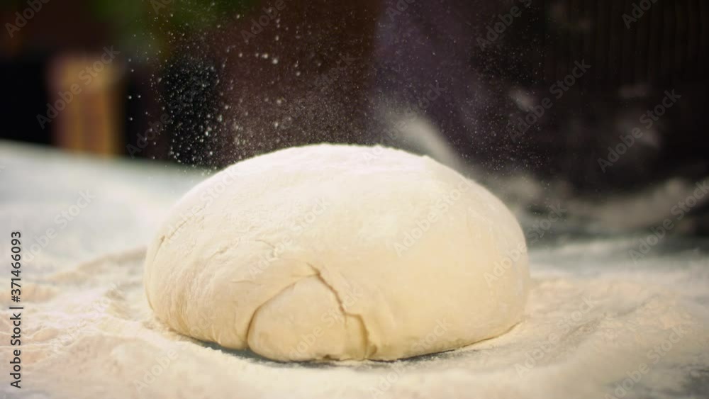 Closeup slow mo shot of hands of chef applying flour on dough Closeup slow mo shot of hands of chef applying flour on dough