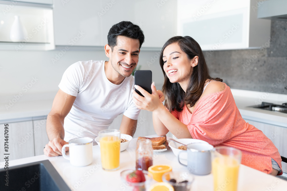 Couple Looking At Mobile Phone During Breakfast