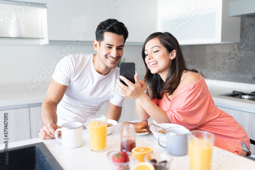 Couple Looking At Mobile Phone During Breakfast